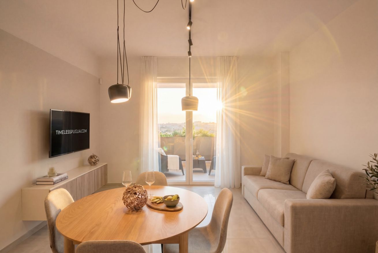 Een moderne woonkamer met een flatscreen televisie, een ronde eettafel met stoelen, een bank en een groot raam met natuurlijk licht.