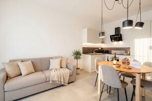 Uma sala de estar moderna com sofá, mesa de jantar e cadeiras. Há uma área de cozinha com fogão e armários.