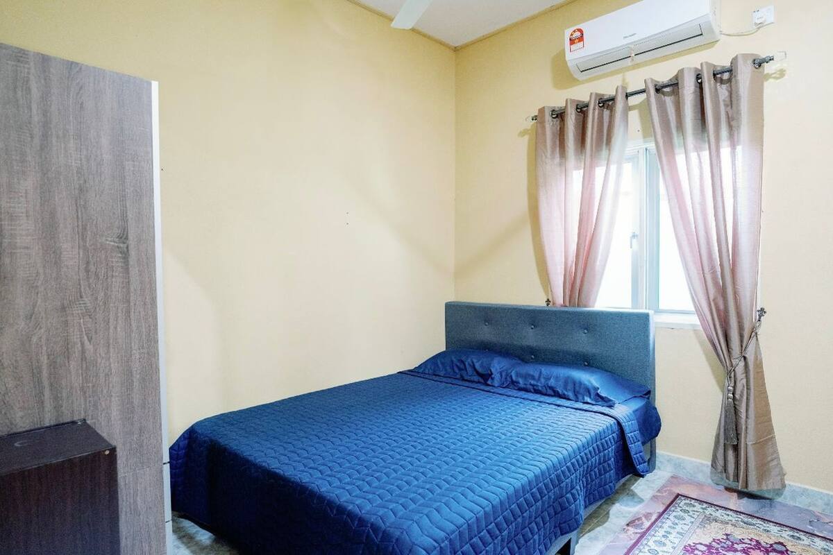 A bedroom with a bed, a window with curtains, an air conditioning unit, and a wooden wardrobe.