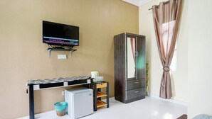Habitación compacta con televisión de pantalla plana en la pared, refrigerador pequeño, escritorio con silla, armario y ventana con cortinas.