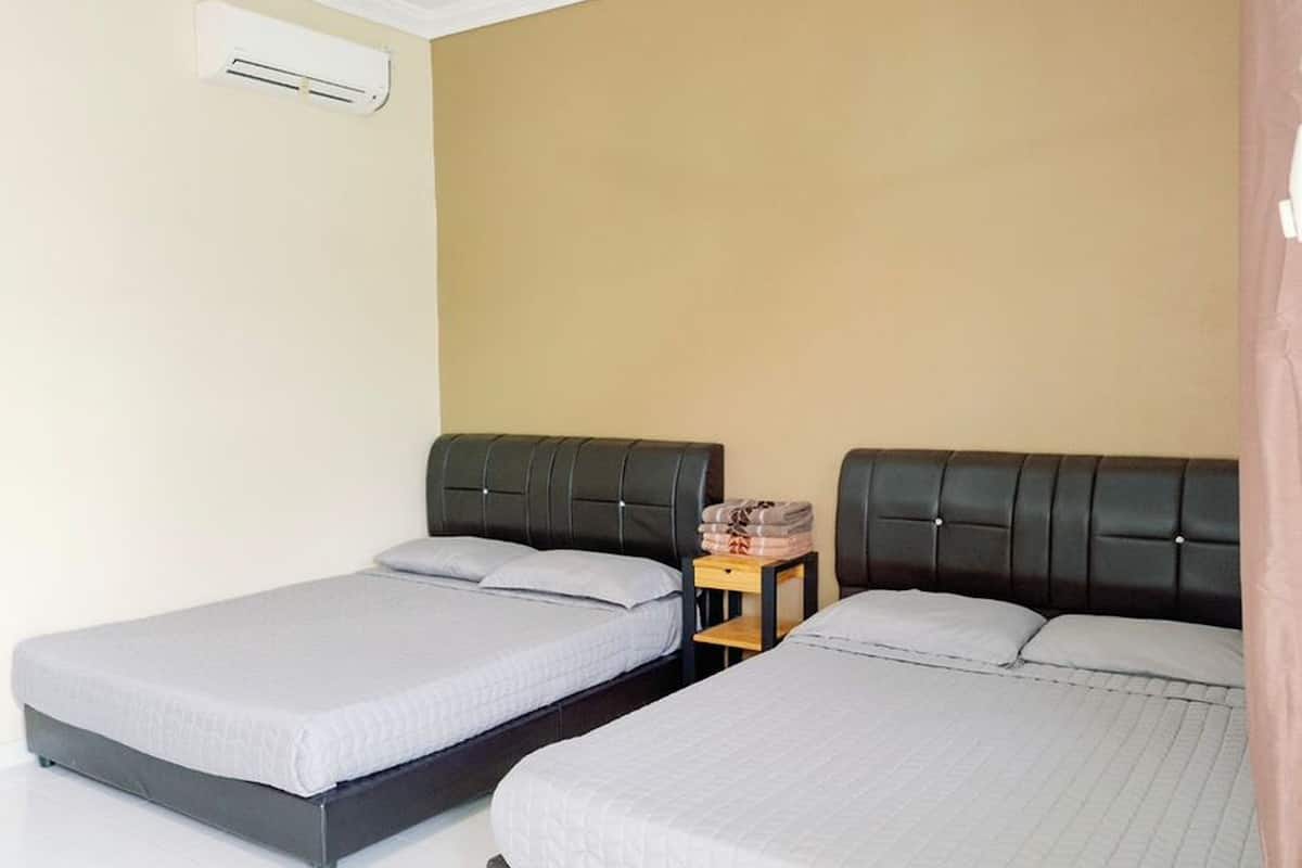 A hotel room with two single beds, a ceiling fan, an air conditioning unit, and a small table with a lamp.