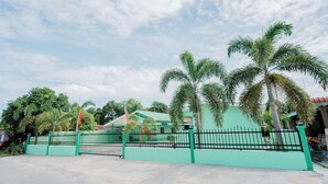 Propiedad amurallada con cerca verde, palmeras y un edificio con techo verde.