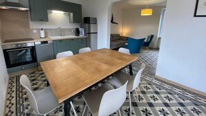 Une cuisine moderne avec un coin repas, comprenant une table en bois et des chaises blanches, un four à micro-ondes et une machine à café.