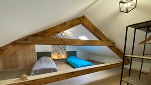 Une chambre située dans un espace de type « loft », avec un plafond en pente, des poutres en bois et une lucarne.
