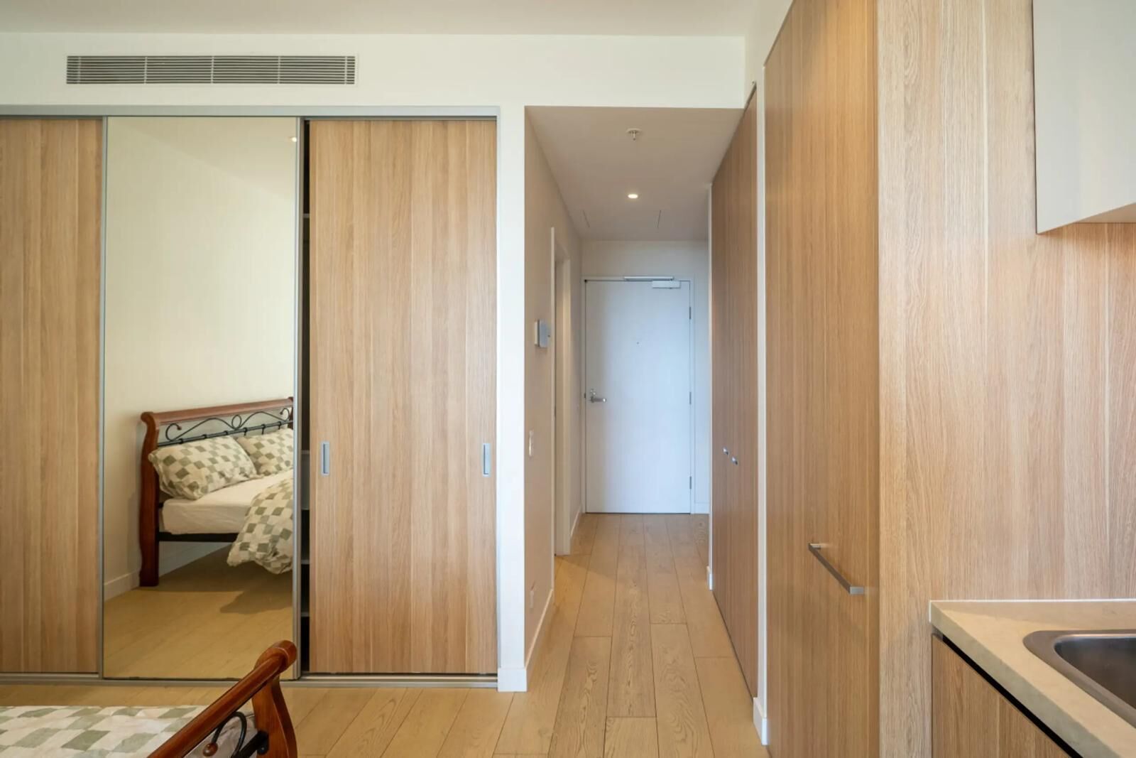 A modern bedroom with a bed, wooden wardrobe, and a kitchen area with a sink.