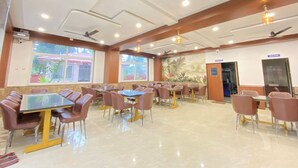 A spacious indoor dining area with multiple tables and chairs, ceiling fans, and large windows providing natural light. - Panchratna Executive Resort (Diveagar)