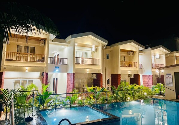 Un hotel con varios balcones, piscina y abundante vegetación.