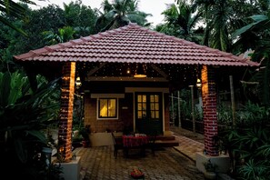 Une petite maison en briques avec un toit en tuiles, une porte d’entrée et une table avec des chaises à l’extérieur.