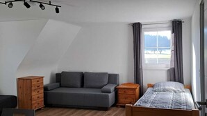 Un dormitorio con una cama, un sof á gris, un aparador de madera y una ventana con cortinas.