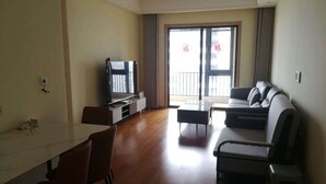 Een moderne woonkamer met een flatscreen televisie, een bank, een eettafel en een balkon met gordijnen.
