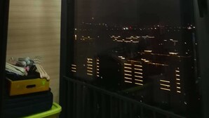 Een raam met uitzicht op een stadsbeeld in de nacht, een metalen hekwerk en een plank met keukengerei.