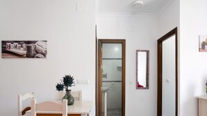 A dining area with a table and chairs, a vase with flowers, a mirror, and a bathroom visible through an open door. - Premium Conil Holiday Apartment (Conil de la Frontera)