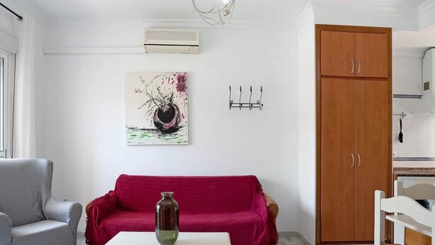 A living room with a grey armchair, a red sofa, a white coffee table, and a wooden wardrobe. - Premium Conil Holiday Apartment (Conil de la Frontera)