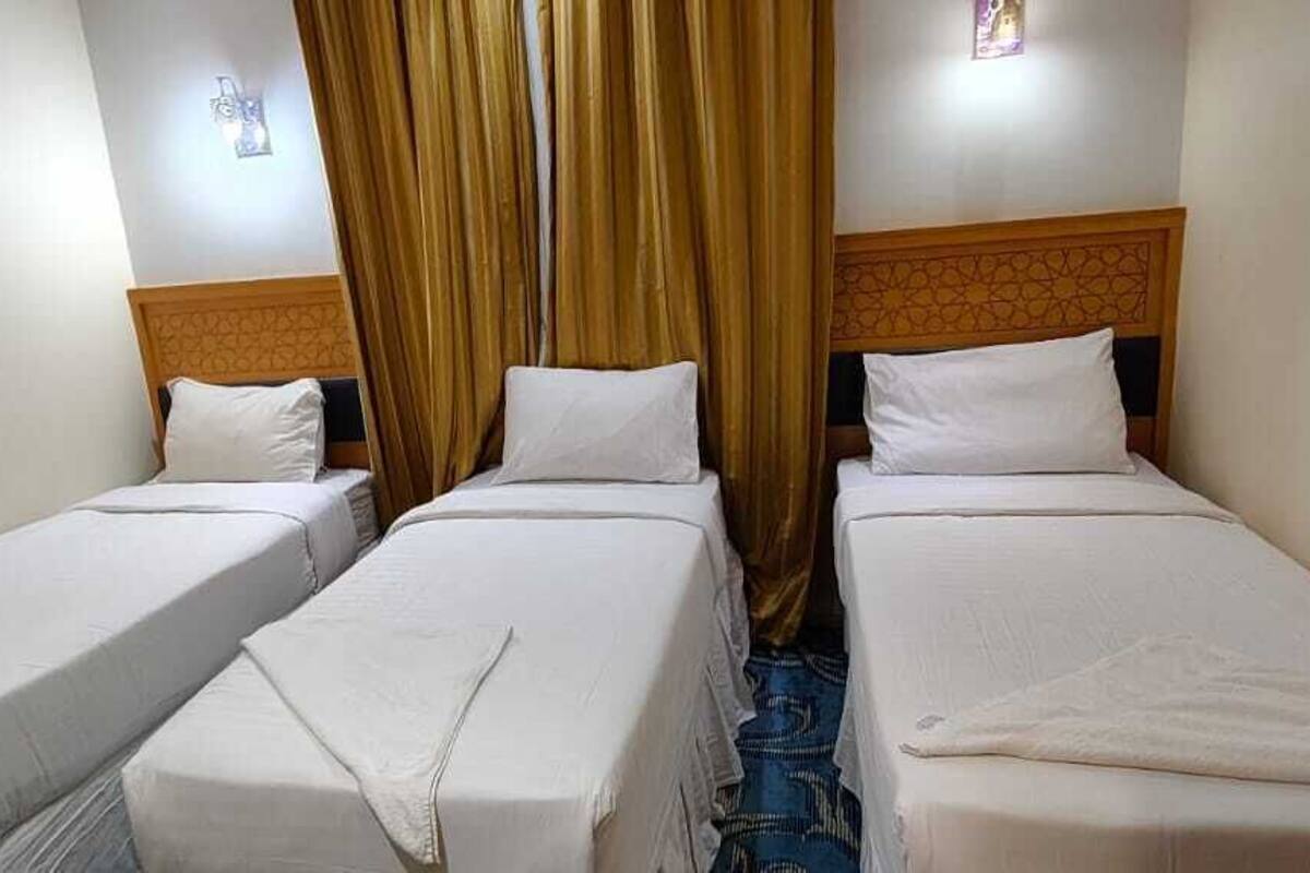 Habitación de hotel con tres camas individuales, cabecera de madera y un separador de cortinas.