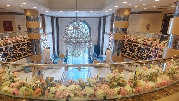 Un hall d’entrée spacieux agrémenté d’un magnifique lustre, d’une balustrade en verre et de compositions florales.