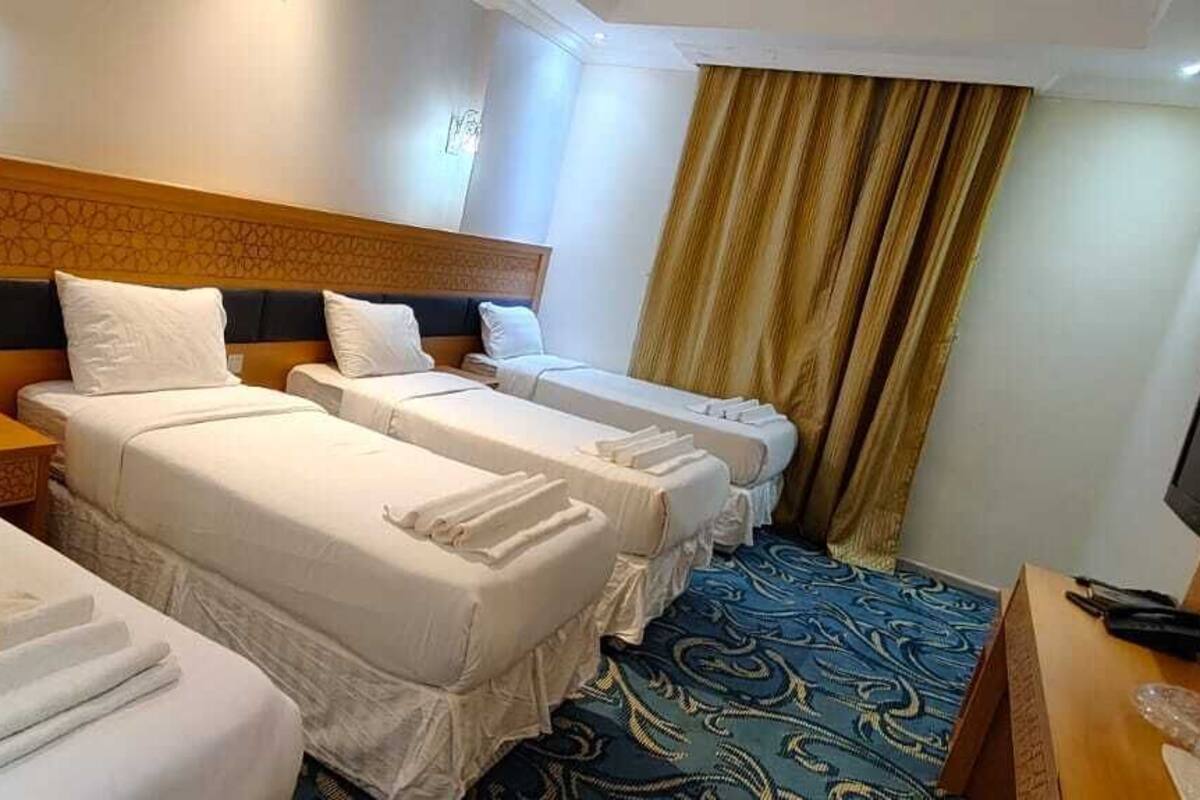 Habitación de hotel con tres camas individuales, cabecero de madera, televisor y alfombra estampada.