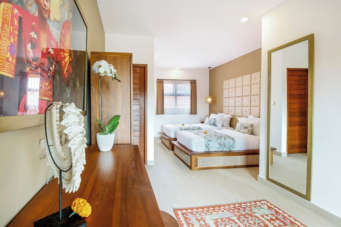 A modern bedroom with a large bed, a small seating area, a mirror, and a decorative plant.