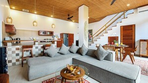 Ein modernes Wohnzimmer mit einem großen grauen Sofa, einem Glastisch und einer Treppe, die in einen oberen Bereich führt.