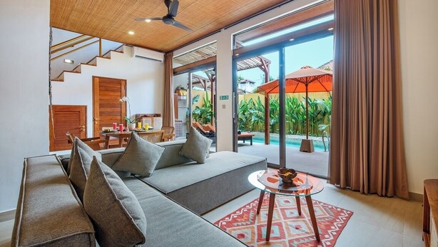 Ein modernes Wohnzimmer mit einer Couch, einem kleinen runden Tisch und Blick auf Pool und Außenbereich.