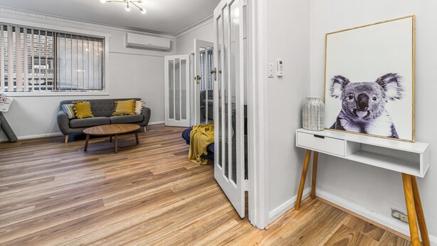 A modern living room with a grey sofa, wooden flooring, and a framed koala artwork on the wall. - Generous size 3BR 1.5Bath Every BD has AC (Oakleigh South)
