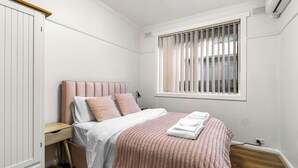 A bedroom with a bed, bedside table, and a window with blinds. - Generous size 3BR 1.5Bath Every BD has AC (Oakleigh South)