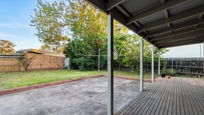 A covered patio area with a wooden deck, a brick wall, and a grassy yard. - Generous size 3BR 1.5Bath Every BD has AC (Oakleigh South)