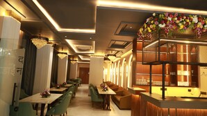Un hall d’hôtel moderne avec un long comptoir d’accueil, des sièges recouverts d’un tissu vert, des lustres et une composition florale décorative.