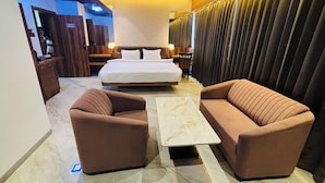 Une chambre d’hôtel moderne avec un grand lit, deux canapés, une table basse en marbre et un téléviseur placé dans un coin.