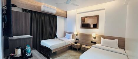 Habitación de hotel con dos camas, un escritorio con tetera y botella de agua, aire acondicionado, ventilador de techo y un espejo en la pared.