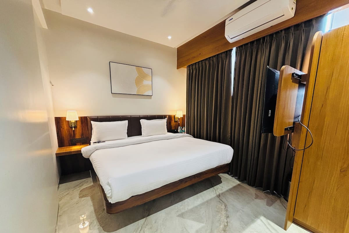 A hotel room with a large bed, a flat-screen TV, a wall-mounted air conditioner, and a painting above the bed.