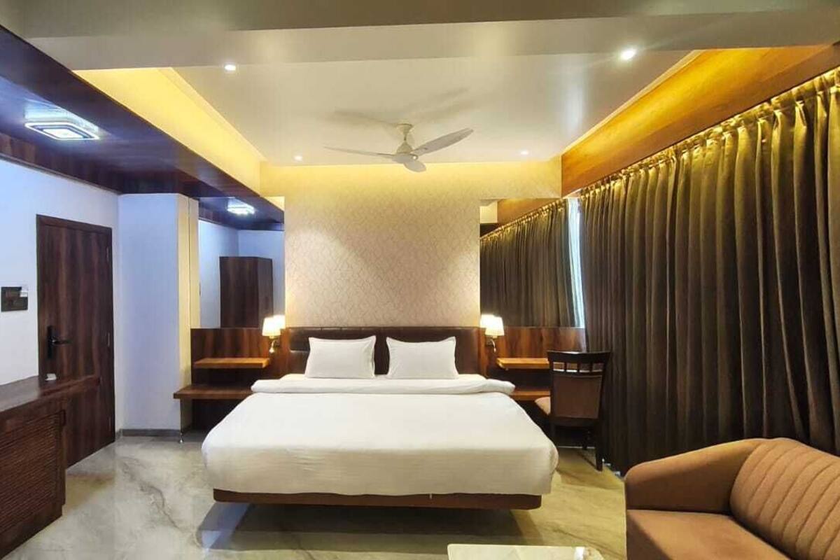A hotel room with a large bed, a ceiling fan, a sofa, and a view of the city.