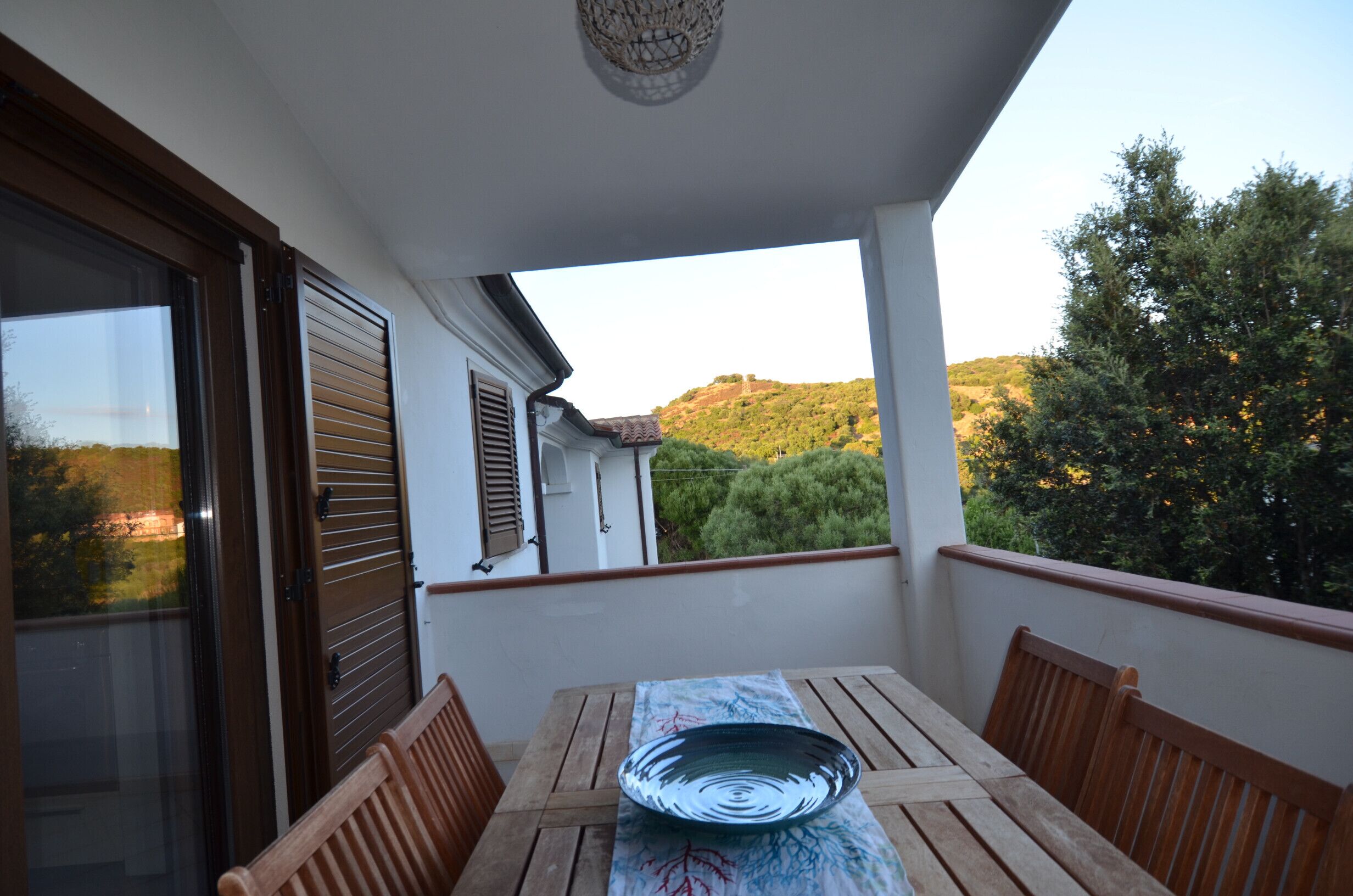 Un balcone con tavolo e sedie, vista su una collina e un edificio con persiane.