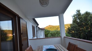 A balcony with a table and chairs, a view of a hill, and a building with shutters. - Fsl-quas01 in San Lorenzo (Budoni)