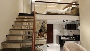 A modern interior with a staircase leading to a loft bedroom, a kitchen with a black countertop, and a living area with a sofa.