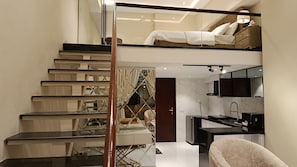 A modern interior with a staircase leading to a loft bedroom, a kitchen with a black countertop, and a living area with a sofa.