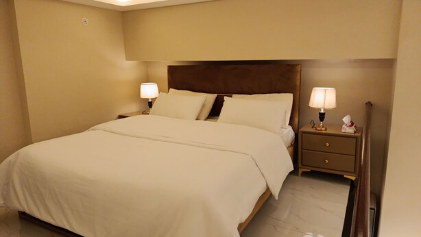 A neatly made bed with white linens, two bedside tables with lamps, and a marble floor.