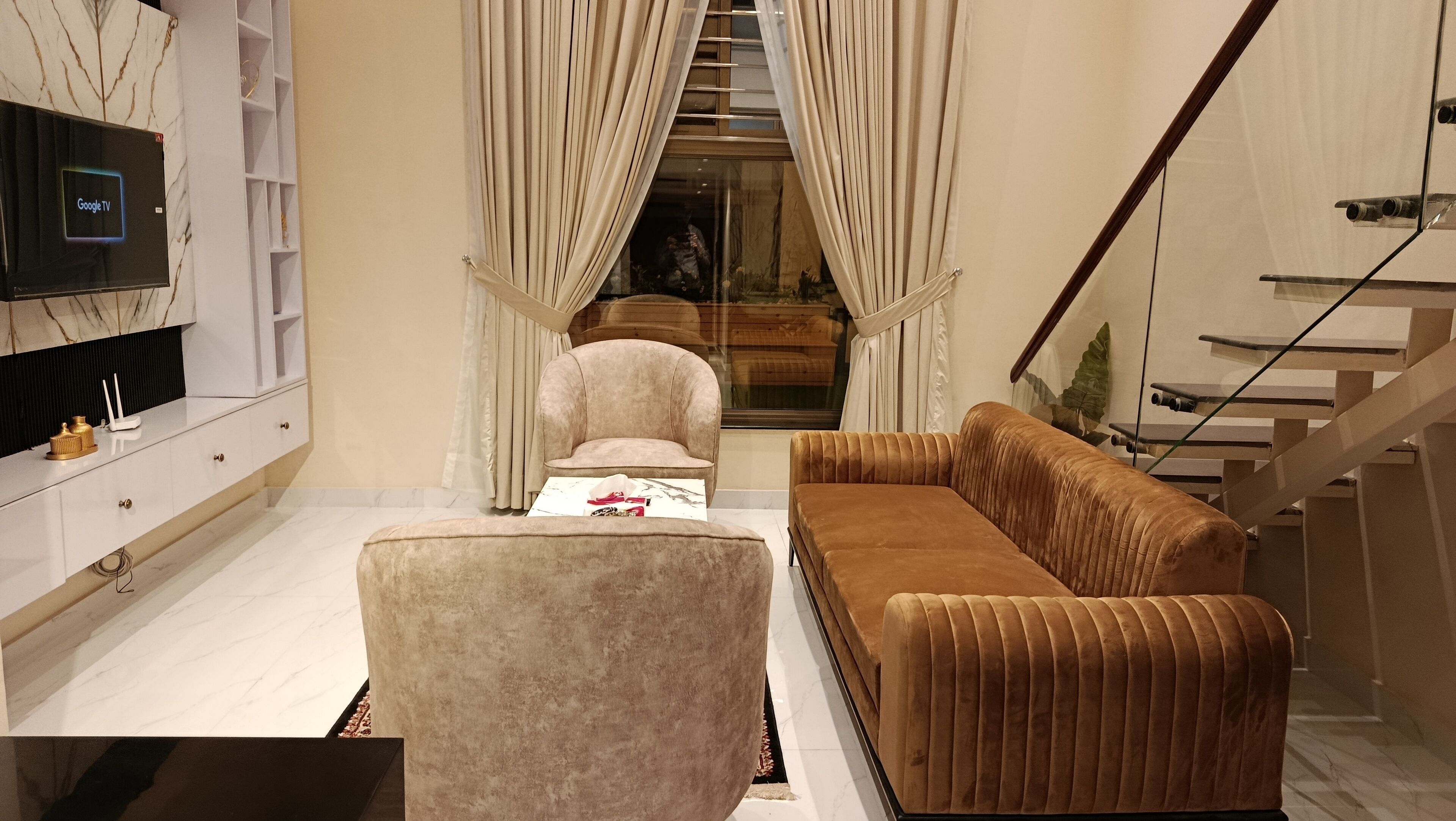 A modern living room with a sofa, armchair, and a TV mounted on a marble wall.