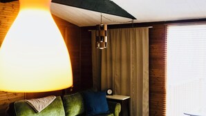 A modern living room with a green sofa, a round wooden coffee table, and a hanging orange pendant light. - Charming Mid-Century Cabin - Warm, Cozy & Scenic (Fort Loudon)