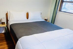 A neatly made bed with white and blue bedding, a wooden headboard, and a bedside table with a lamp. - Charming Mid-Century Cabin - Warm, Cozy & Scenic (Fort Loudon)