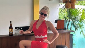 A woman in a red dress sitting at a bar with a bottle of beer and a glass of water. - Eros Hotels Green house (Unawatuna)