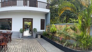 A building with a curved balcony, a paved courtyard, and various plants. - Eros Hotels Green house (Unawatuna)