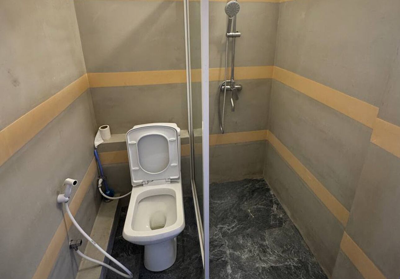 A small, narrow bathroom with a toilet, a shower, and a marble floor.
