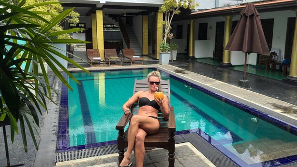 A woman sitting by a pool with a chair and a potted plant nearby. - Eros Hotels Green house (Unawatuna)