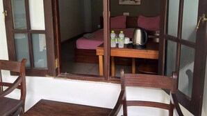A room with a bed, a table with a kettle, and a chair. - Eros Hotels Green house (Unawatuna)