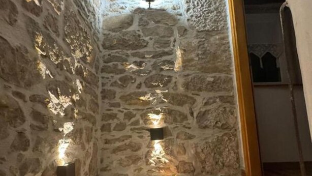 Un couloir étroit aux murs de pierre, doté d’un éclairage intégré et d’un banc en bois.