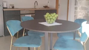 Un coin repas avec une table ronde et des chaises bleues, un saladier de pommes vertes sur la table, et une cuisine en arrière-plan.