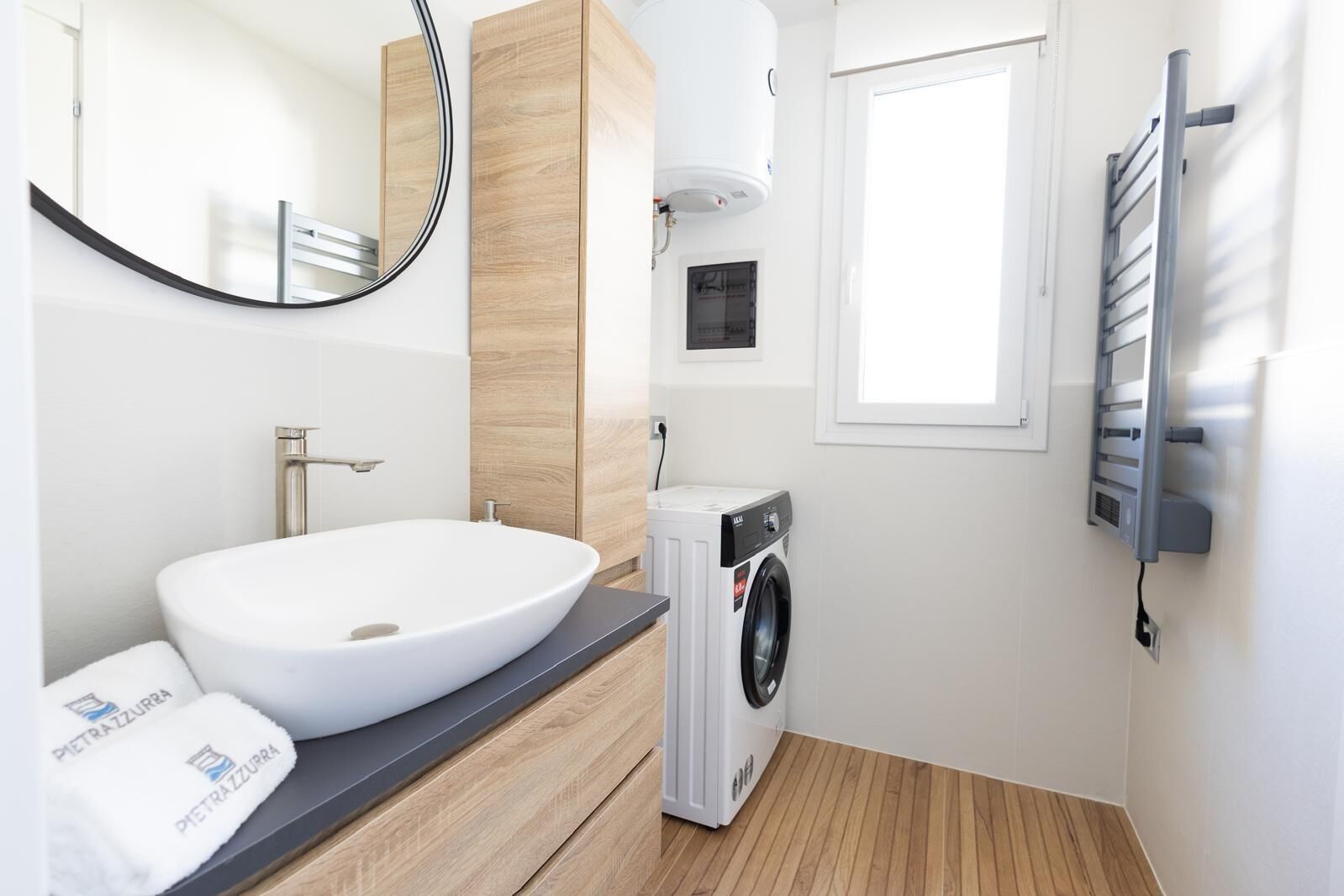 A modern bathroom with a white sink, a mirror, a built-in washing machine, and a towel rack.