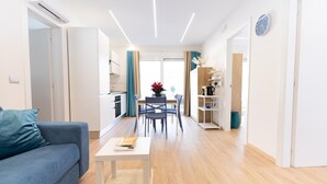A modern living room with a blue sofa, a coffee table, and a dining area with chairs and a table.