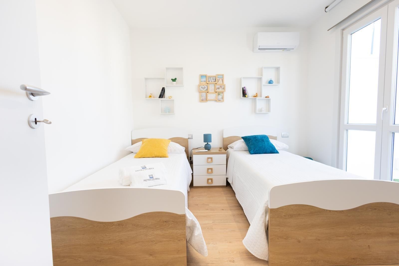 Een hotelkamer met twee bedden, een houten vloer, witte muren en een raam.