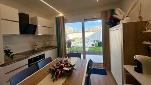 A modern kitchen with a dining area, a view of the outdoor garden, and a small house model on the shelf.